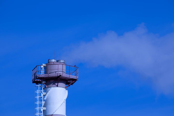 The steaming tube or pipe of the plant, factory or thermal power station on the background of clear blue sky