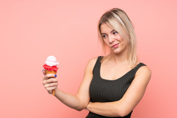 Young blonde woman with a cornet ice cream over isolated pink background with sad expression
