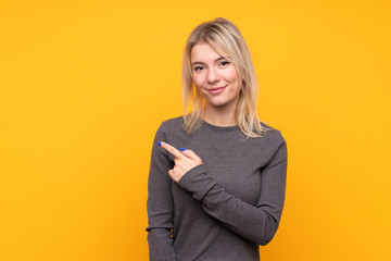 Young blonde woman over isolated yellow background pointing to the side to present a product