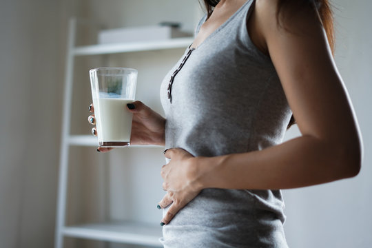 Slim woman with stomach ache and pain holding a glass of milk. Dairy intolerant, Lactose intolerance, allergy, health care concept