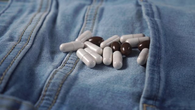 A handful of medical capsules on blue jeans. White and brown. Dolly shot. Contraceptive use and treatment of impotence