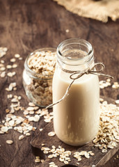 Oat flakes milk, non dairy alternative plant based drink in glass, wooden rustic kitchen table, copy space