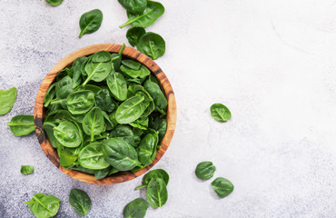 Fresh baby spinach leaves in wooden bowl on gray stone table. Top view, copy space