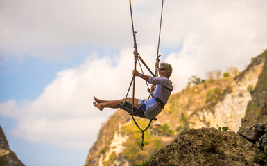 mature attractive and happy woman on with grey hair enjoying amazing rock cliff view from swing feeling young and free swinging carefree having beautiful retirement