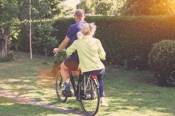 Obraz premium Rear view of senior couple riding a bicycle together - leisure, having fun and ecological transport concept
