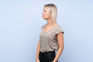 Young blonde woman over isolated blue background looking side