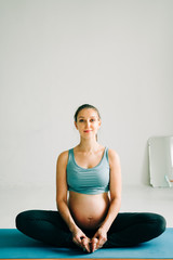 Fototapeta premium a young pretty pregnant girl in sports clothes is doing yoga, doing asana Baddha Konasana on the Mat in the Studio