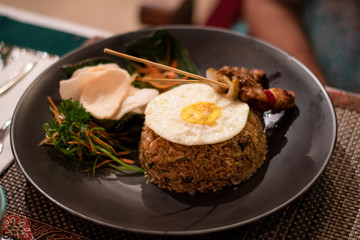 Nasi goreng, a traditional balinese food served during the dinner in a black plate in a restaurant in Bali