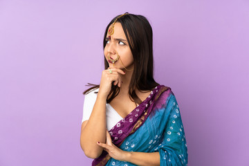 Young Indian woman isolated on purple background having doubts and with confuse face expression