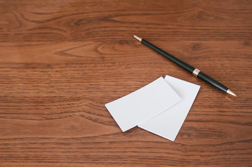 Empty business cards lie on a brown wooden table. Next to them is a black ballpoint pen. Idea for business.