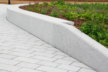 Moderner Garten und Landschaftsbau: Gestaltung eines Hochbeets umgeben von einer Mauer entlang eines Gehwegs aus Naturstein Platten