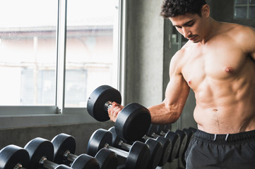Fototapeta na wymiar Strong muscular man workout in gym doing exercises at biceps. Weight training concept.