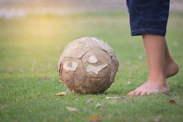 Close-up of boy Barefoot playing football on the green grass ground 