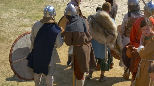 Girls carry water in jugs to the Vikings before the fight. Medieval warriors in armor drink water.