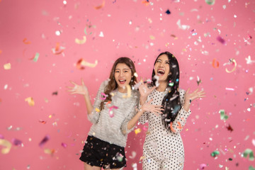 Obraz na płótnie Canvas Portrait of a cheerful beautiful Asian womanl wearing dress standing standing under confetti rain and celebrating isolated over pink background