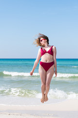 Fototapeta na wymiar Young girl woman in red bikini bathing suit sunglasses jumping up with ocean sea green water in background in Santa Rosa Beach and horizon