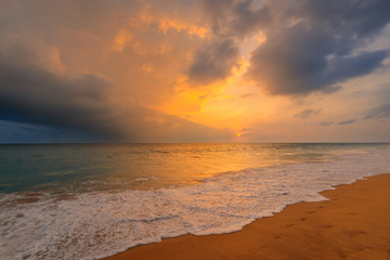 Fototapeta na wymiar Foamy waves on sandy ocean beach under a beautiful sunset sky with clouds on Sri Lanka island.
