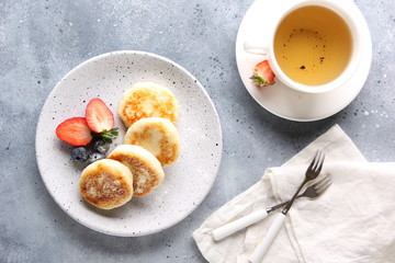 Concept of Russian and Ukrainian cuisine. Cottage cheese pancakes. Cheesecakes with fresh berries with a cup of tea on a light grey background. Background image, copy space