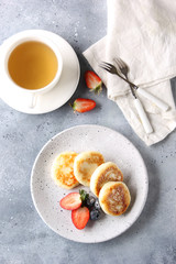 Concept of Russian and Ukrainian cuisine. Cottage cheese pancakes. Cheesecakes with fresh berries with a cup of tea on a light grey background. Background image, copy space