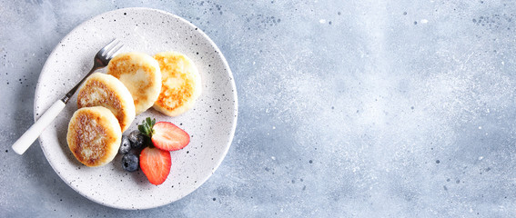 Concept of Russian and Ukrainian cuisine. Cottage cheese pancakes. Cheesecakes with fresh berries on a light grey background. Background image, copy space