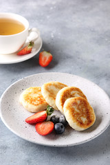 Concept of Russian and Ukrainian cuisine. Cottage cheese pancakes. Cheesecakes with fresh berries with a cup of tea on a light grey background. Background image, copy space