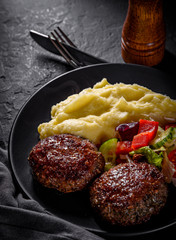burger with mashed potatoes and vegetables salad on a black plate on Dark grey black slate background