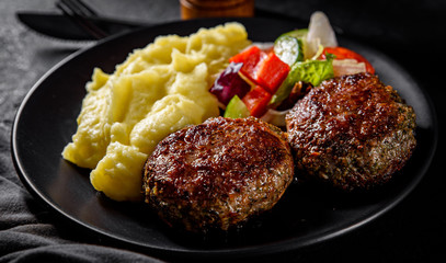 burger with mashed potatoes and vegetables salad on a black plate on Dark grey black slate background