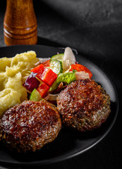 burger with mashed potatoes and vegetables salad on a black plate on Dark grey black slate background