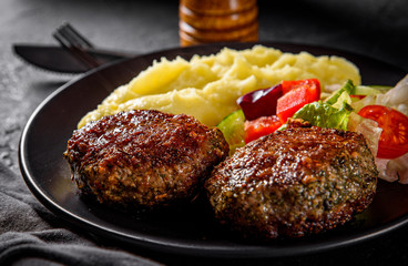 burger with mashed potatoes and vegetables salad on a black plate on Dark grey black slate background