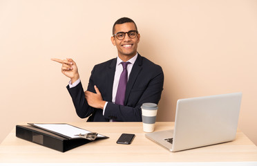 Young business man in his office with a laptop and other documents pointing finger to the side