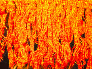 orange, red thread fibers of a piece of fabric hang