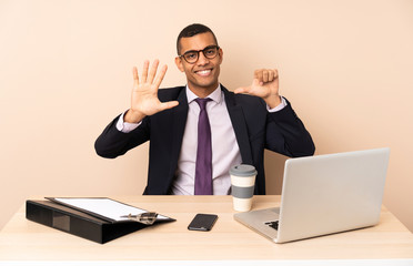 Young business man in his office with a laptop and other documents counting six with fingers