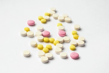 The concept of pills for treatment. Multi-colored white,  yellow, pink tablets on a white isolate background . Copy space. Place for text.