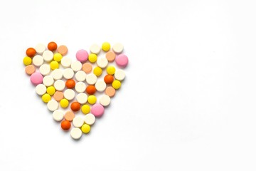 The concept of pills for treatment. Multi-colored white, orange, yellow, pink pills in the shape of a heart  on a white isolate background. Copy space