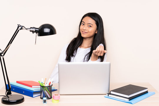 Student asian girl in a workplace with a laptop isolated on beige background inviting to come with hand. Happy that you came
