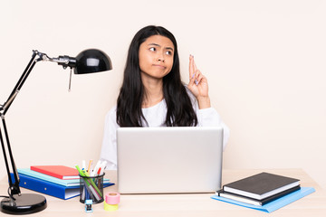 Student asian girl in a workplace with a laptop isolated on beige background with fingers crossing and wishing the best