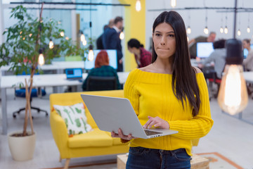 Young female business woman standing with laptop and posing  at work while the Group of a young business multiethnic people brainstorming and discussing business plan on meeting.