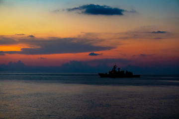 Silhouette of warship sails in the sea when the red light of civil twillight brace upon the sea surface.