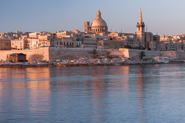 Fototapeta premium Valletta with Our Lady of Mount Carmel church and St. Paul's Anglican Pro-Cathedral at sunrise as seen from Sliema, Valletta, Malta