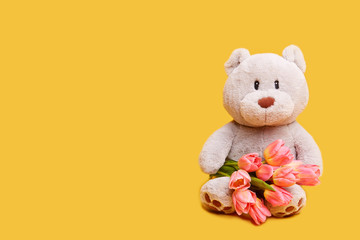 Soft toy bear with a bouquet of pink tulips on a yellow background. Сoncept for Women's Day 