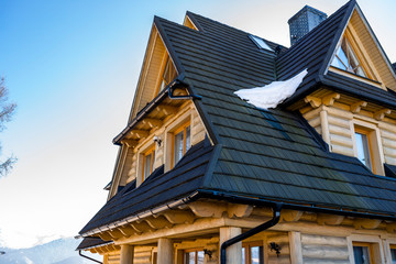 Wooden house in the Polish mountains with a dark blue wooden roof covered with snow.
