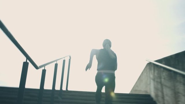 Energetic athletic woman exercising on the stairs in urban area. Handheld tracking action shot. Celebrating on the top.