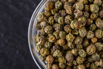 green peppercorns on dark slate stone background