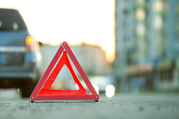 Red emergency triangle stop sign and broken car on a city street.