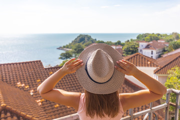 Fototapeta premium girl with a pink dress and hat on the balcony against the sea and tiled roof