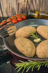 Raw cutlet in breadcrumbs. Frying pan, induction cooker, spices, olive oil, salt, tomato, rosemary, garlic, vertical photo, mirror surface.
