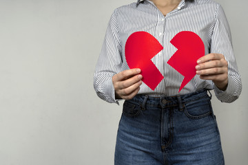 Female showing red broken paper heart, symbolizes the end of love, divorce, breakup, loss of feelings for your loved one. End or breaking relations. Heart health problem.