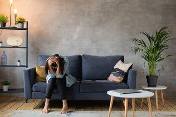 Worried woman sitting on couch at home. Frustrated confused female feels unhappy, problems in personal life, quarrel break up with boyfriend and unexpected pregnancy concept