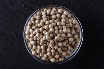 white peppercorns in glass bowl on stone background
