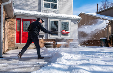 Man Removing Snow with a Red Shovel in Front of a House - Powered by Adobe